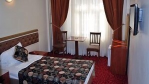 Una habitación de hotel con una cama, una mesita con dos sillas, un televisor y una alfombra roja.