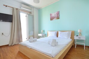 A hotel room with a bed, a flat-screen TV, a painting, a nightstand, and a window with curtains. - A cute & comfortable 2 bedroom apartment (Piraeus)