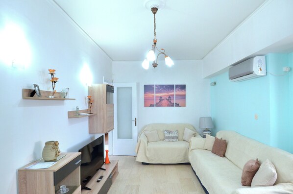 A living room with a sofa, TV, wooden cabinet, and a painting on the wall. - A cute & comfortable 2 bedroom apartment (Piraeus)