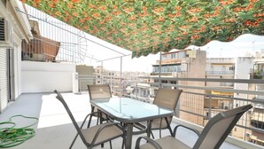 A balcony with a glass table and chairs, a green garden hose, and a decorative floral canopy. - A cute & comfortable 2 bedroom apartment (Piraeus)