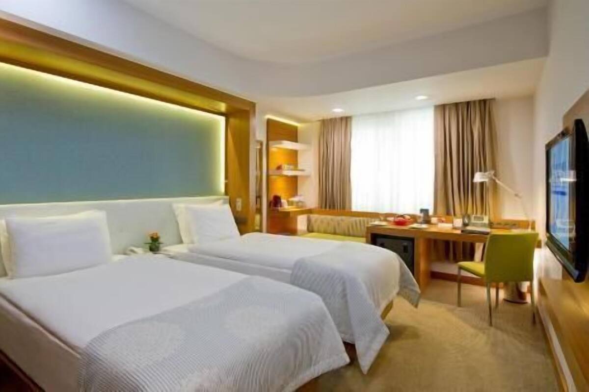 A hotel room with two beds, a desk, a chair, a TV, and a window with curtains.