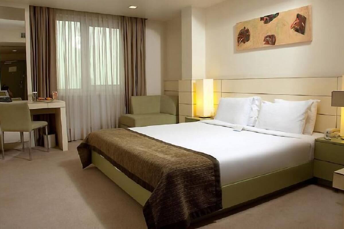 A hotel room with a bed, a desk, a chair, a lamp, and a painting on the wall.
