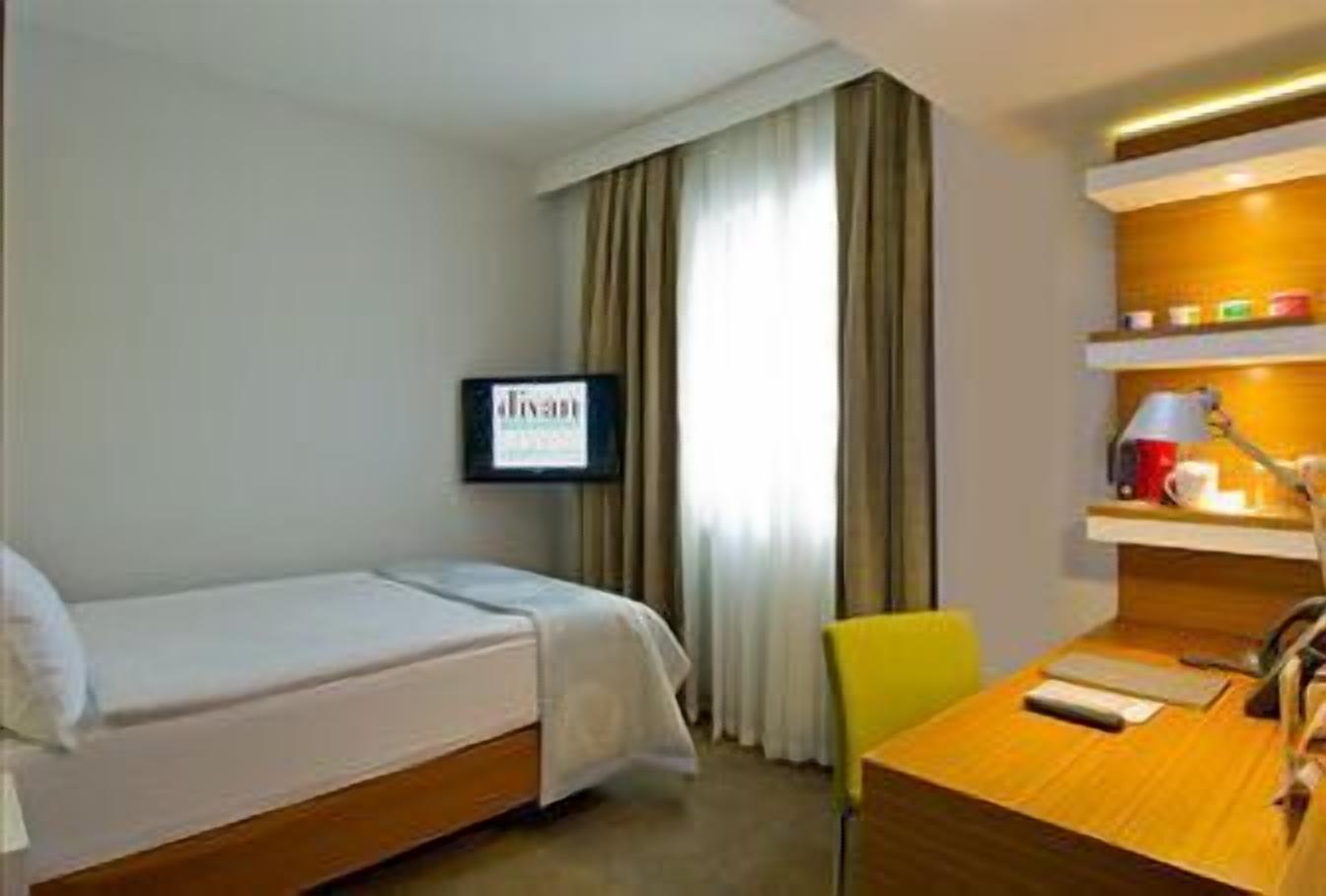 A hotel room with a bed, a desk, a chair, a television, and a window with curtains.