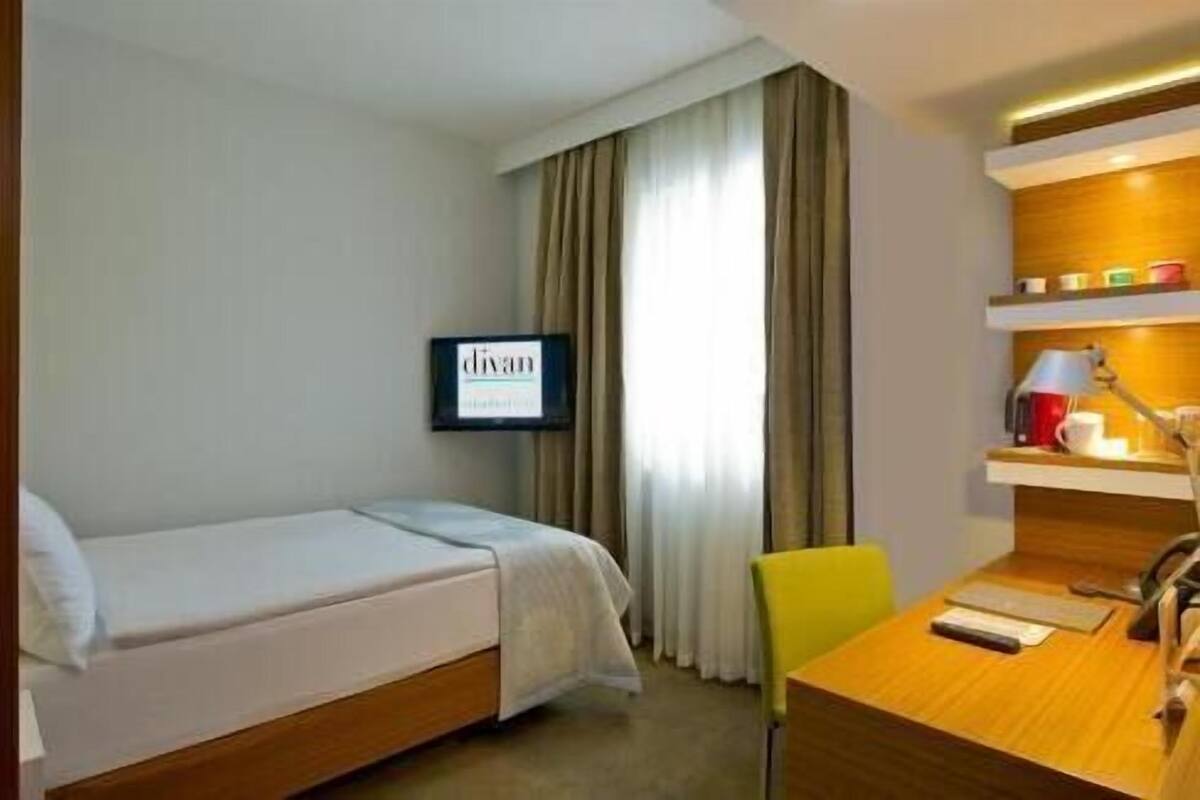 A hotel room with a bed, a desk, a chair, a TV, and a window with curtains.