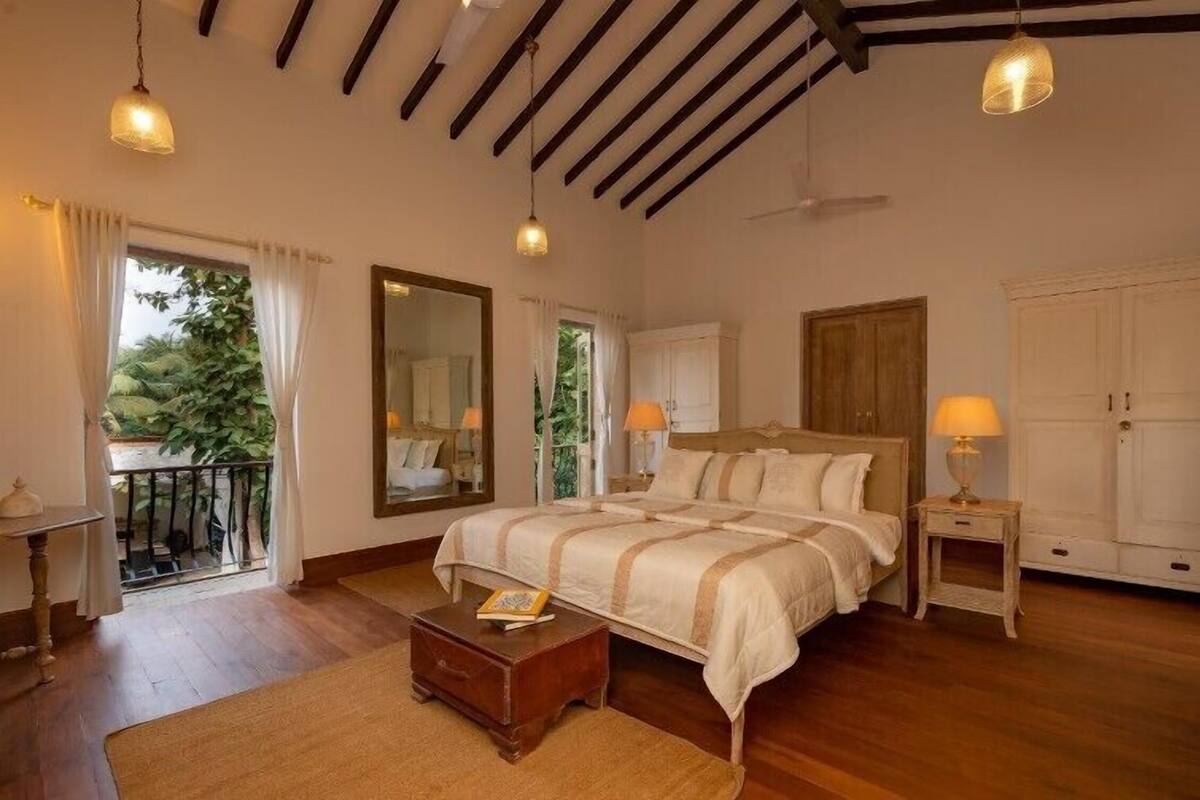 A bedroom with a large bed, bedside tables, a mirror, and a view of the outdoors.