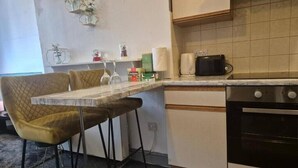 A compact kitchen with a dining area, including a table and two chairs, a coffee maker, and a stove. - Glams one bedroom apartment (Wolverhampton)