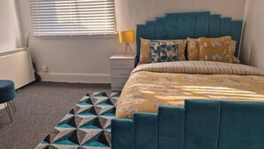 A bedroom with a bed, a bedside table, a lamp, and a geometric-patterned rug. - Glams one bedroom apartment (Wolverhampton)