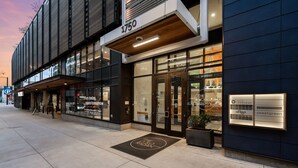 En modern byggnad med en stor glasfasad, ett väl synligt adressskylt och en välkomstmatta med byggnadens namn.