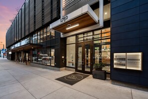 A modern building with a large glass storefront, a visible address sign, and a welcome mat with the building's name. - New Listing! Walkable Denver Luxury | Rooftop Pool | City Views (Denver)