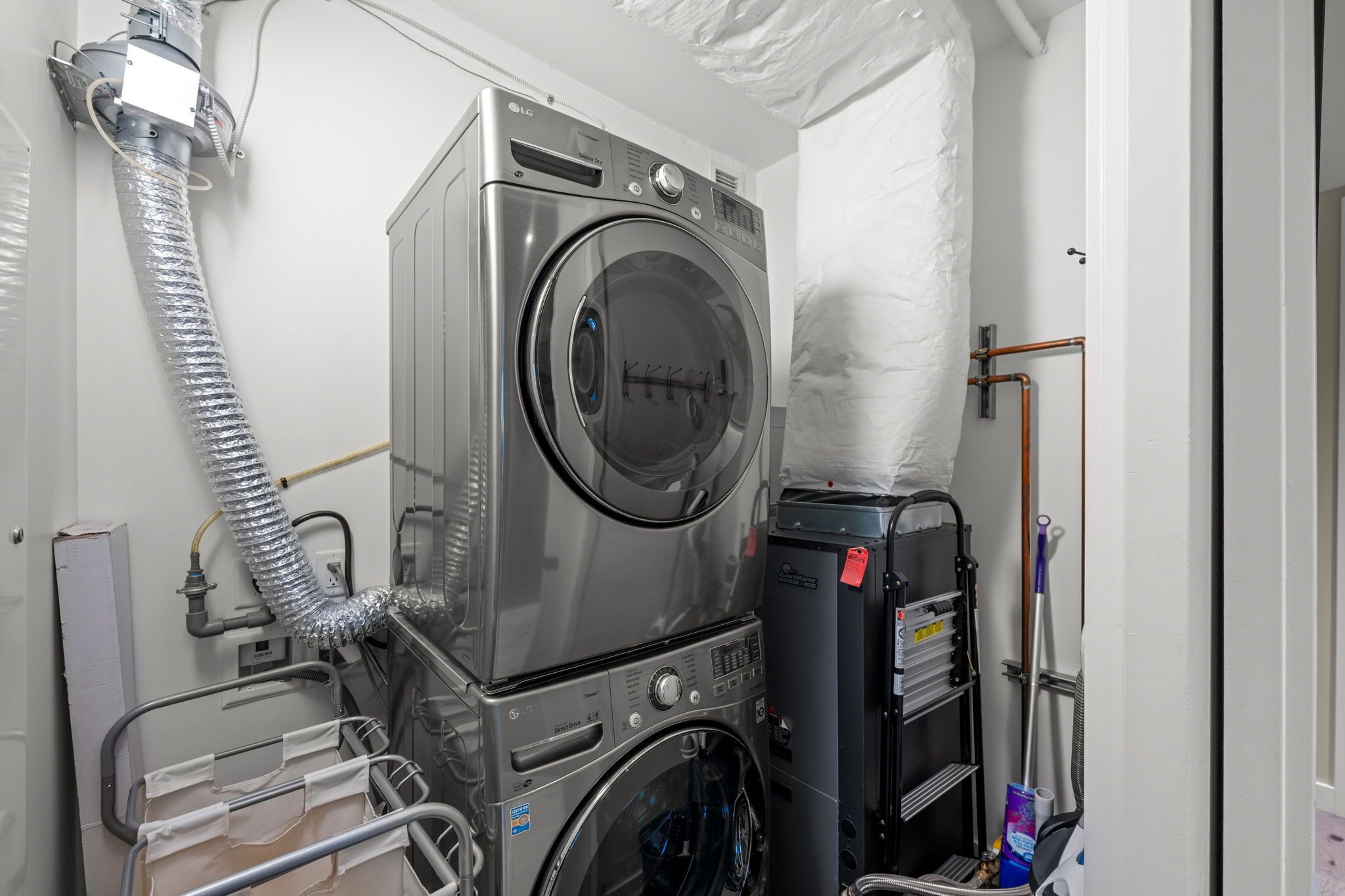 A compact laundry room with stacked washers and dryers, a hose for water connection, and a metal rack with cleaning supplies.