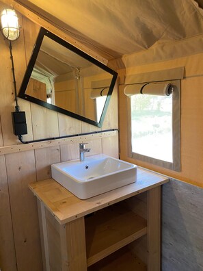 A wooden cabin bathroom with a white sink, a mirror, and a window with a towel hanging. - Luxury Glamping Near the Frisian Waters (De Veenhoop)