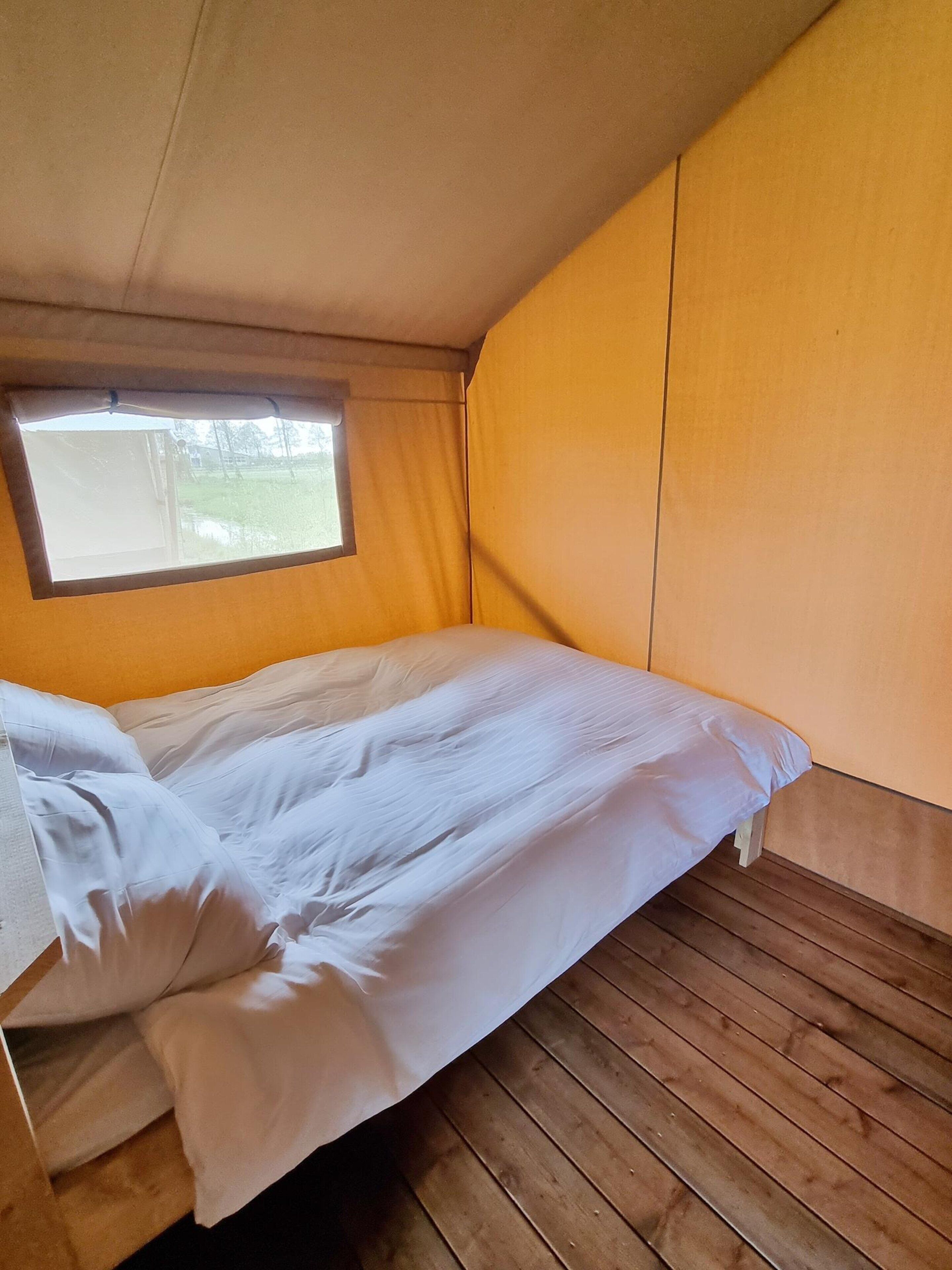 A single bed with white bedding in a room with wooden flooring and a window.