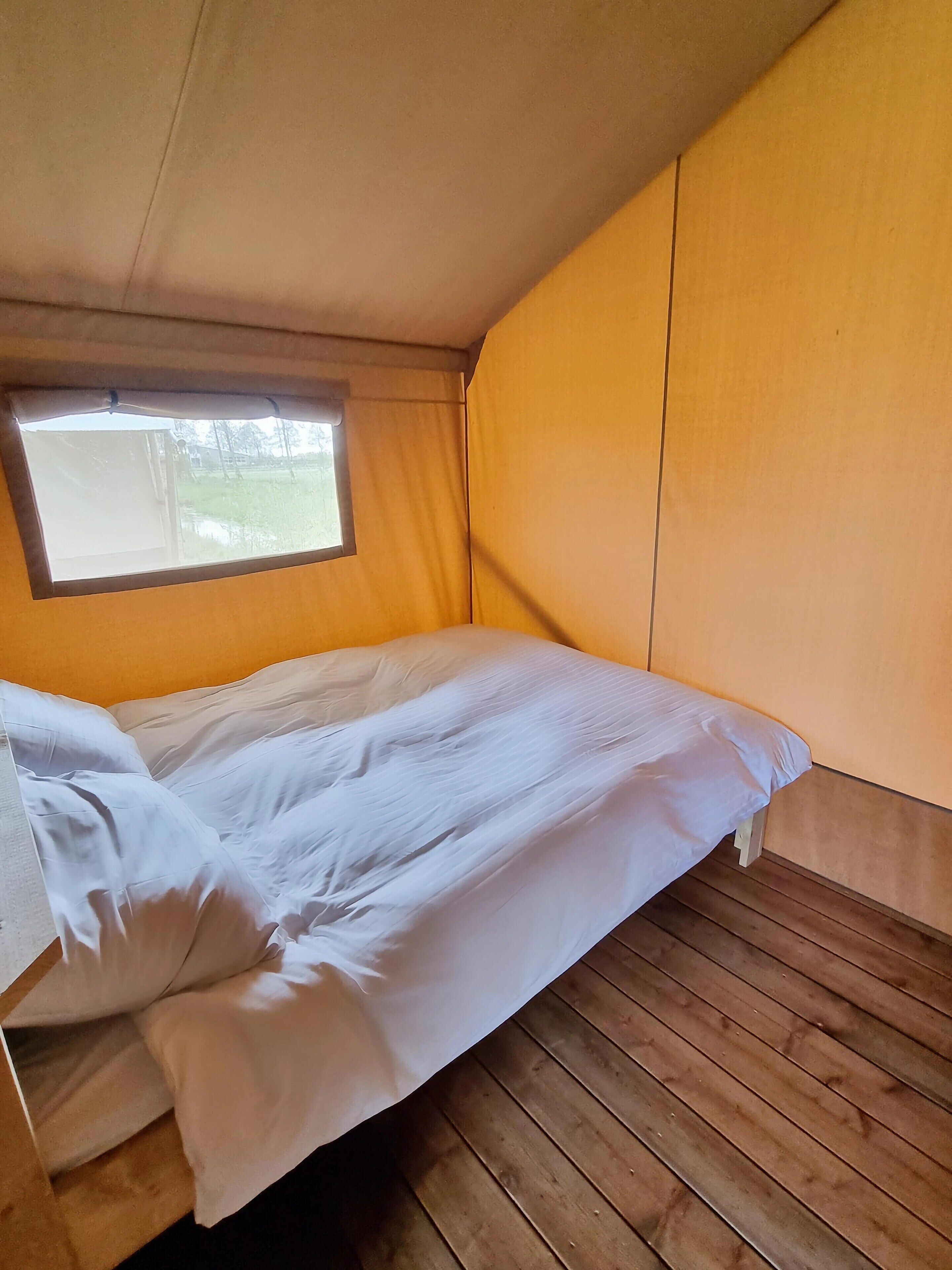 A single bed with white bedding in a room with wooden flooring and a window.