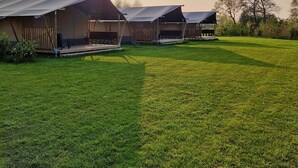 A row of simple, single-story buildings with flat roofs, likely used for accommodation or storage, set against a backdrop of a grassy field and trees. - Luxury Glamping Near the Frisian Waters (De Veenhoop)