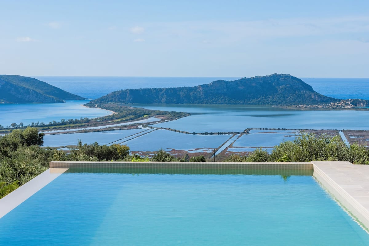Ein Schwimmbecken mit Blick auf eine Küstenlandschaft und sanfte Hügel in der Ferne.