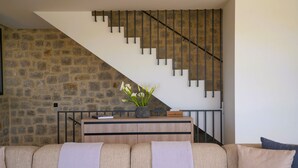 Un salon avec un mur en pierre, un escalier, un canapé et une petite table sur laquelle est posée une plante.