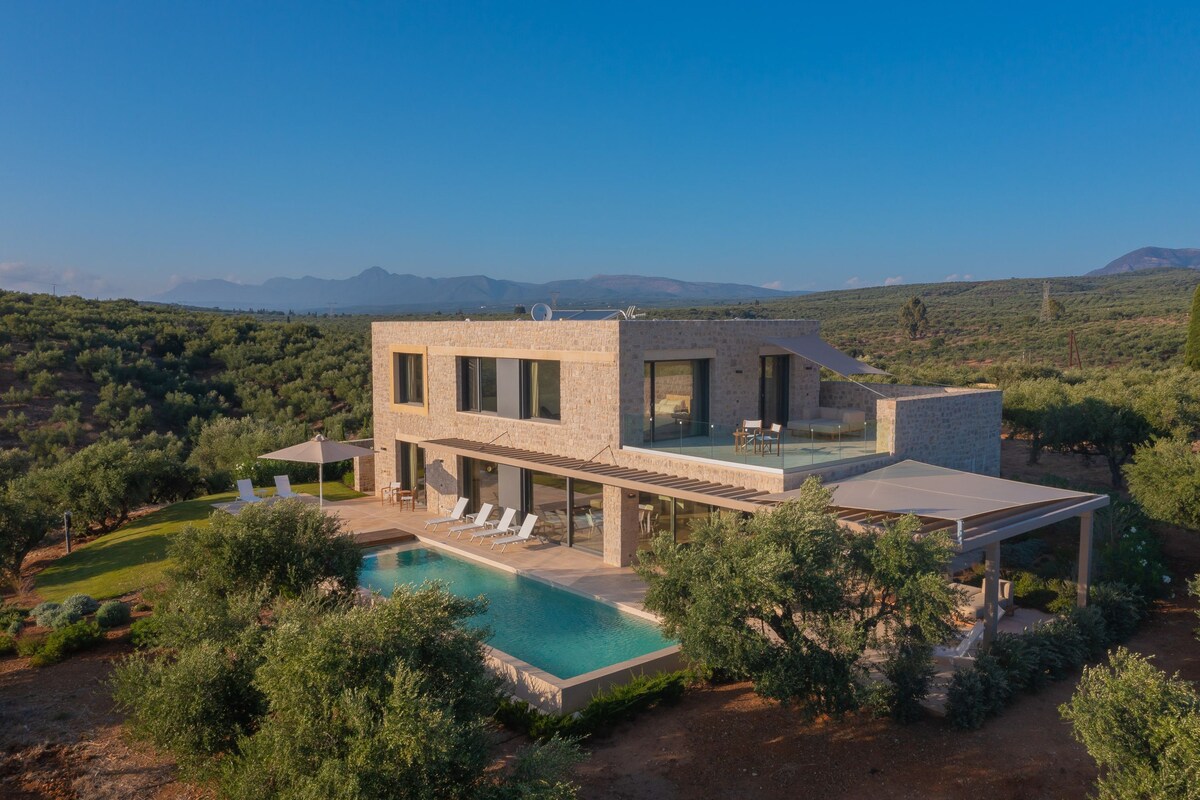 Une maison moderne avec une piscine, entourée de verdure et avec des montagnes en toile de fond.