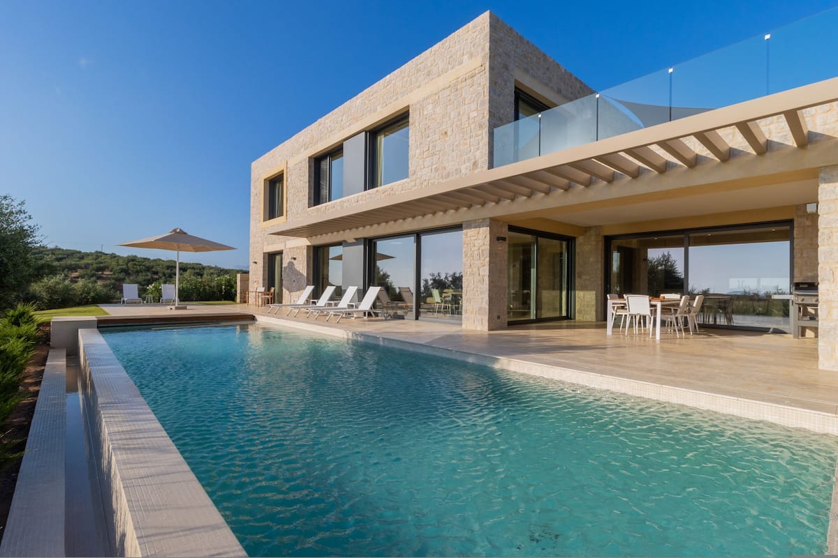 Ein modernes Haus mit Swimmingpool, Sitzgelegenheit im Freien und einer Glasbrüstung.