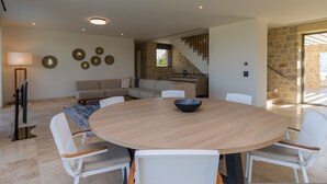 Un salon moderne avec une table ronde en bois, des chaises blanches, un canapé et un escalier menant à un autre niveau.