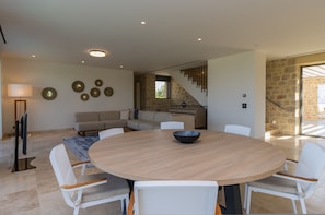 A modern living room with a round wooden table, white chairs, a sofa, and a staircase leading to another level. - Messinian Nest (Pylos-Nestoras)