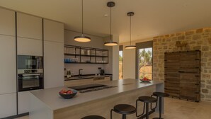 Une cuisine moderne dotée d’un îlot central, de tabourets de bar, de luminaires suspendus et d’un mur d’accent en pierre.