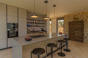 A modern kitchen with a central island, bar stools, pendant lighting, and a stone accent wall. - Messinian Nest (Pylos-Nestoras)
