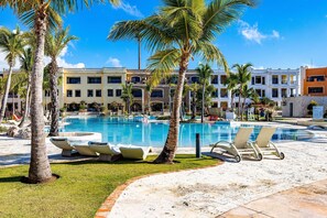 A pool area with lounge chairs, palm trees, and a building with balconies. - Paradise Cove Cap Cana Monthly Rental (La, Altagracia)