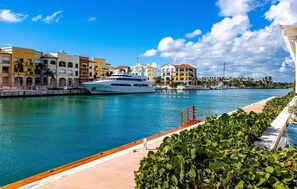 A waterfront marina with a large yacht docked, buildings with balconies, and a clear sky. - Paradise Cove Cap Cana Monthly Rental (La, Altagracia)