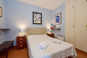 A neatly made bed with towels, a bedside lamp, a framed artwork on the wall, and a wardrobe. - Sunny Haven at the Village Square (Palafrugell)