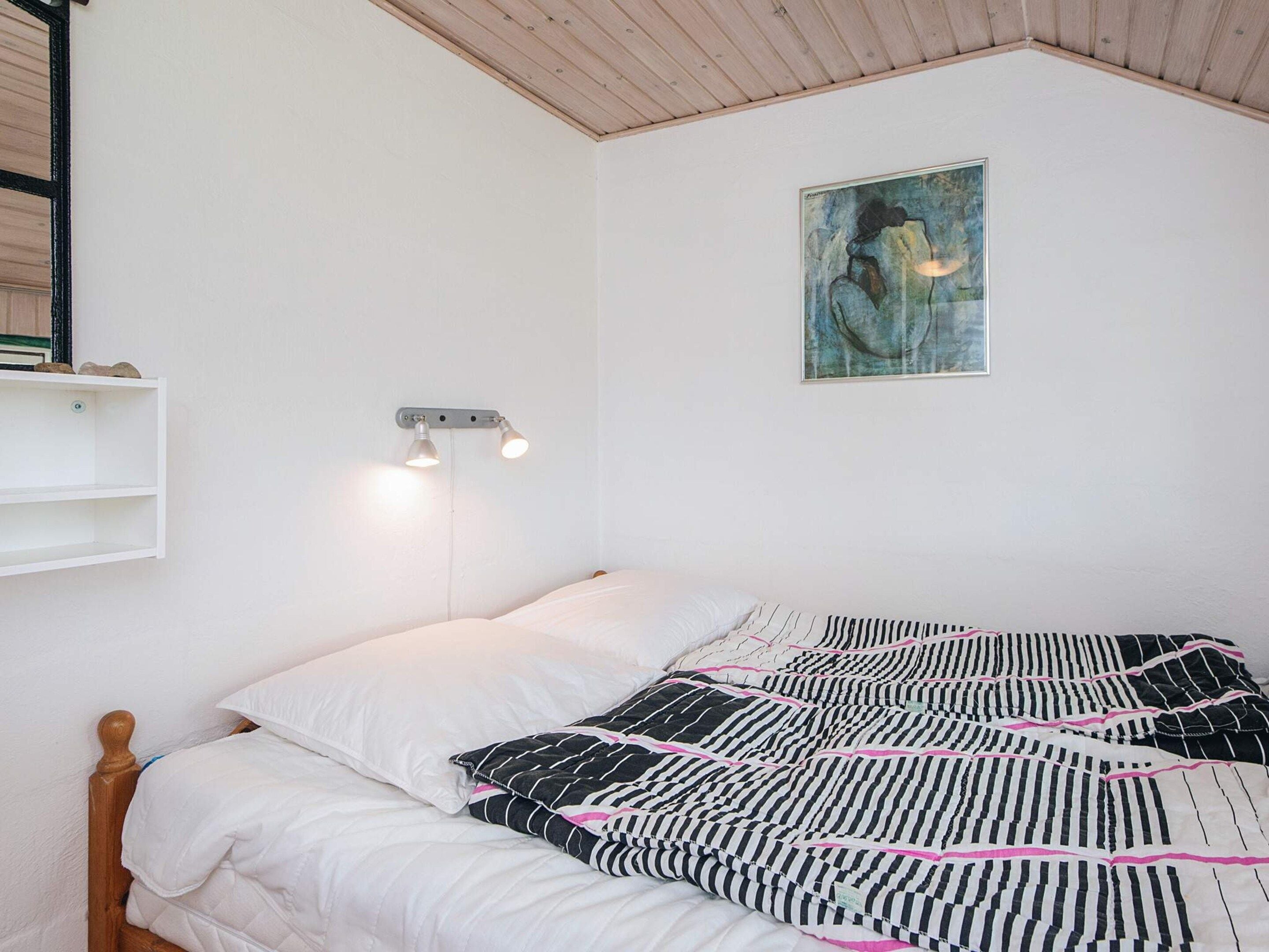 A bedroom with a bed, a wall-mounted light fixture, and a painting.