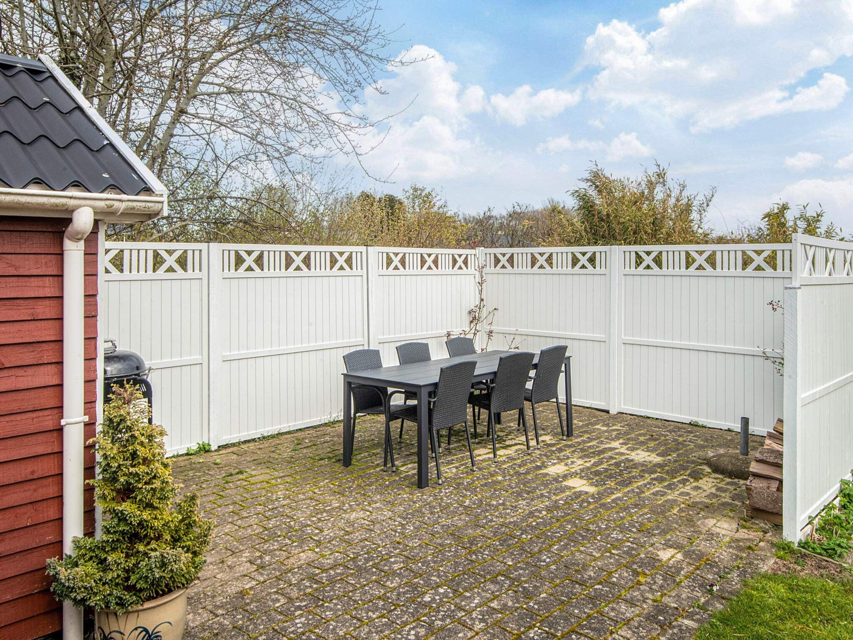 A patio with a table and chairs, a white fence, and a small potted plant.