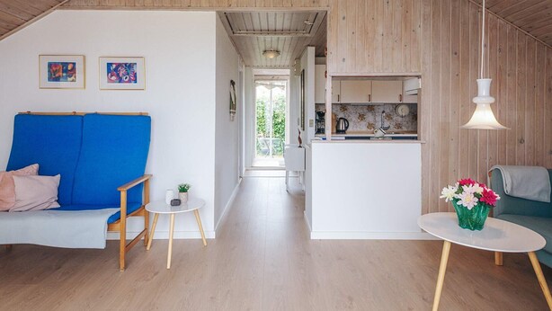 Ein Loft-Zimmer mit Holzbalkendecke, einem blauen Sofa, einem kleinen Tisch mit Blumenvase und einer Küchenzeile.