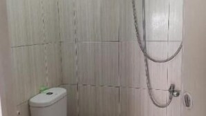 Um banheiro pequeno com vaso sanitário, chuveiro e suporte de papel higiênico na parede.