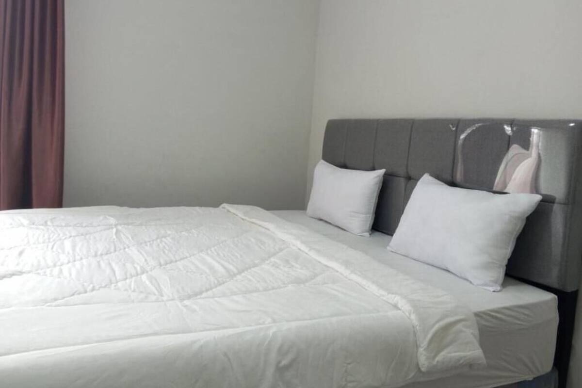 A bed with a grey headboard, white bedding, and a brown curtain.