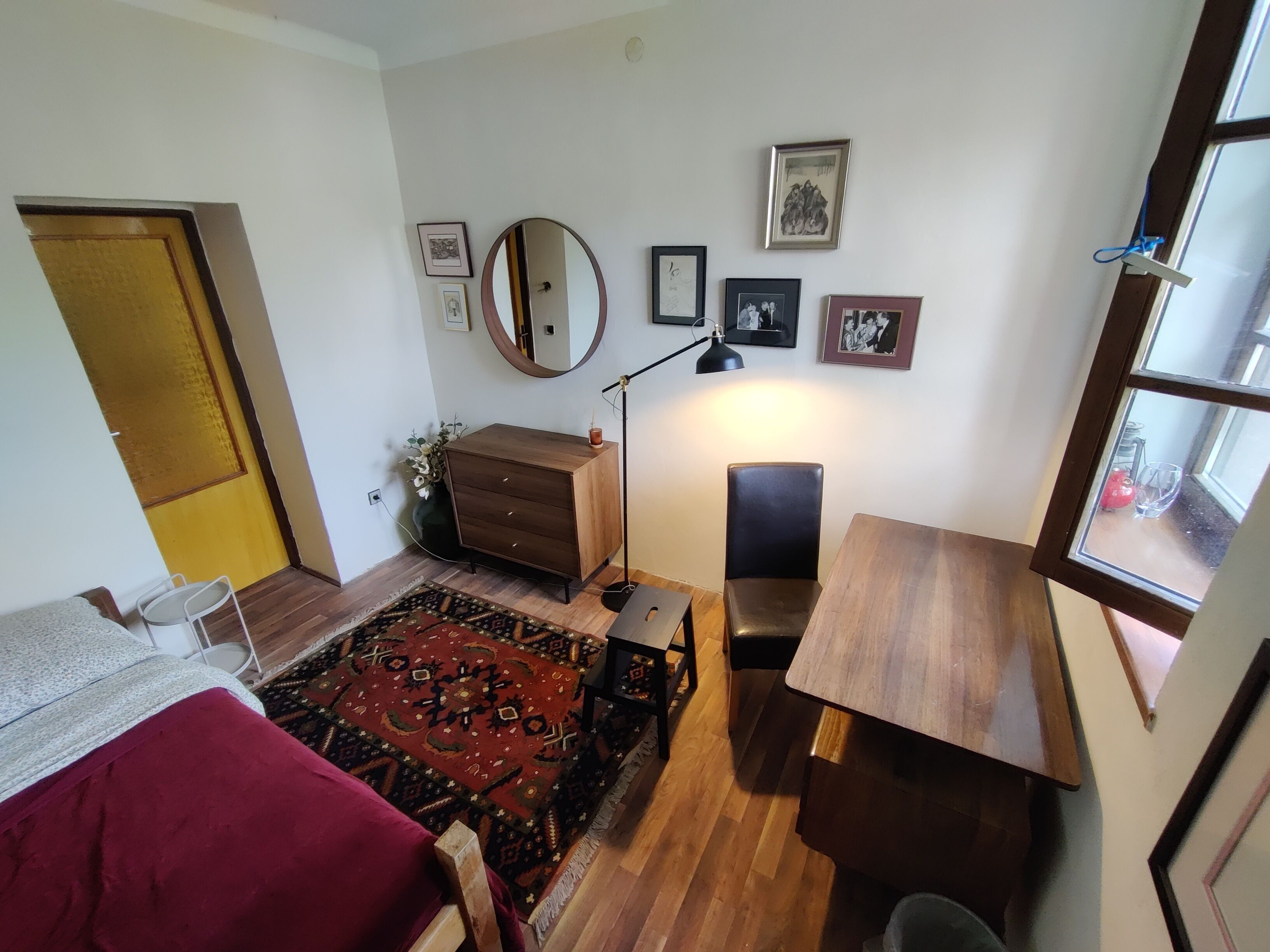 Ein Zimmer mit einem Bett, einem Schreibtisch, einem Stuhl, einer Kommode, einem Spiegel und einem Fenster.