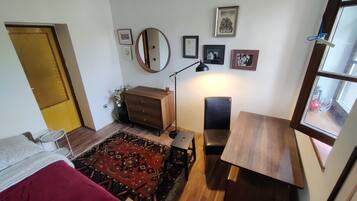 Ein Zimmer mit einem Bett, einem Schreibtisch, einem Stuhl, einer Kommode, einem Spiegel und einem Fenster.