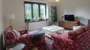 A living room with a sofa set, a coffee table, a TV, and a window with plants. - Spacious, two-bedroom garden apartment. Free gated parking. (Český Krumlov 1)
