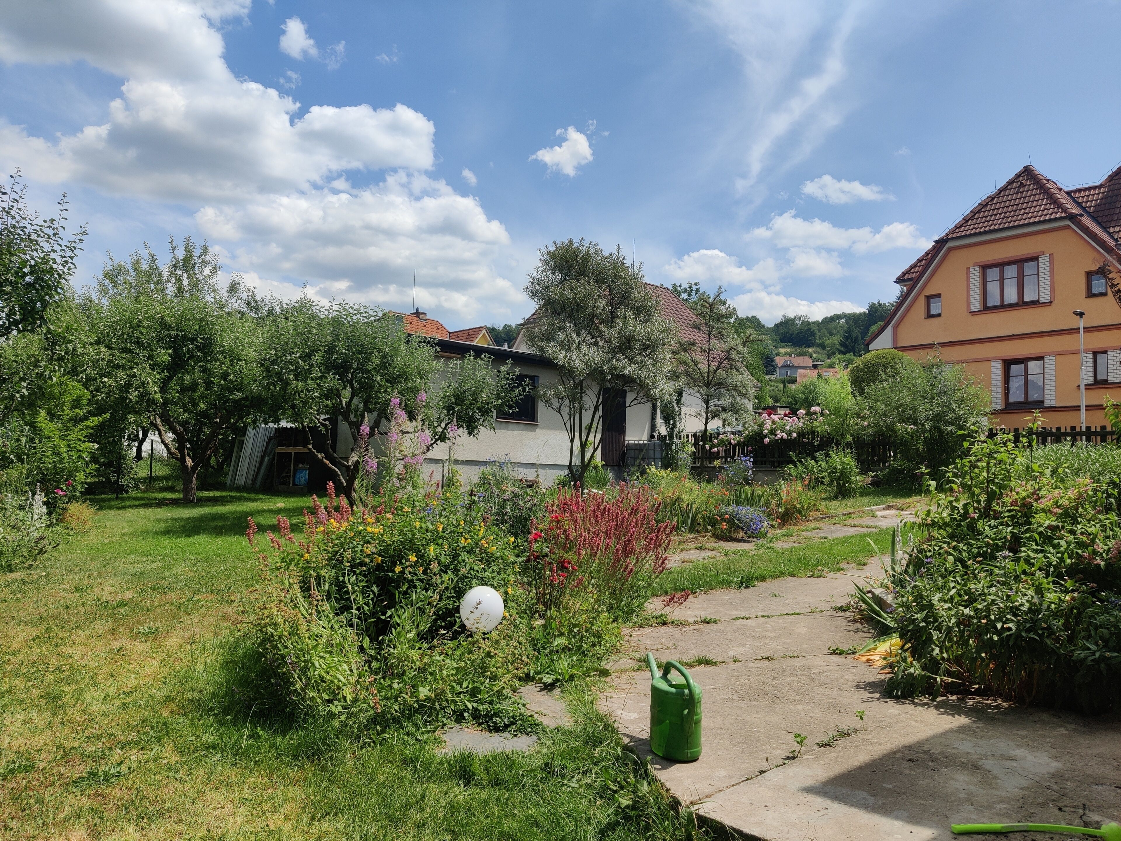 Een tuin met een pad, een wit bolvormig object en een groene gieter.