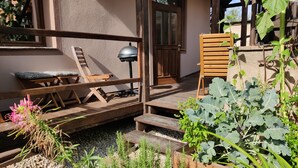 A wooden deck with a bench, a door, and a garden area with plants and a small table. - Spacious, two-bedroom garden apartment. Free gated parking. (Český Krumlov 1)