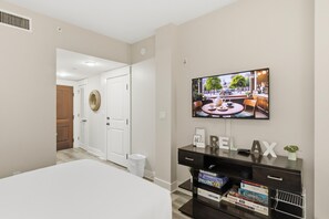 A hotel room with a bed, a TV mounted on the wall, a desk with a plant, and a door leading to another room. - Pilot House Studio in Sandestin Golf and Beach Resort! (Miramar Beach)