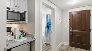 Eine Küche mit Mikrowelle, Toaster und Kaffeemaschine, einer Holztür und einer Dusche mit blauer Duschvorhang.