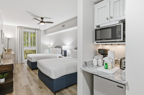 A hotel room with two beds, a kitchenette, a ceiling fan, and a window with curtains. - Pilot House Studio in Sandestin Golf and Beach Resort! (Miramar Beach)