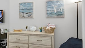 Ein Zimmer mit einem Holzkasten, zwei an der Wand befestigten Bildern von Segelbooten, einem Fernseher und einem Korb mit Zeitschriften.
