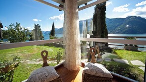 A room with a large window overlooking a lake and mountains, wicker furniture, and a wooden floor. - Villa Meraviglia  (Olgiasca)