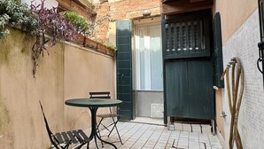 Ein schmales Außenareal mit Tisch und Stühlen, einer Tür und einem gefliesten Boden.