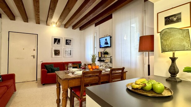 Ein Wohnzimmer mit einem roten Sofa, einem Holzesstisch und einem an der Wand montierten Fernseher.