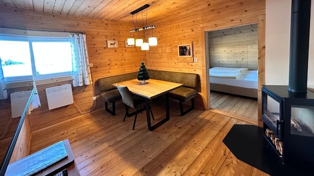Et interiør af en træhytte med spiseplads, bænk, pejs og seng.