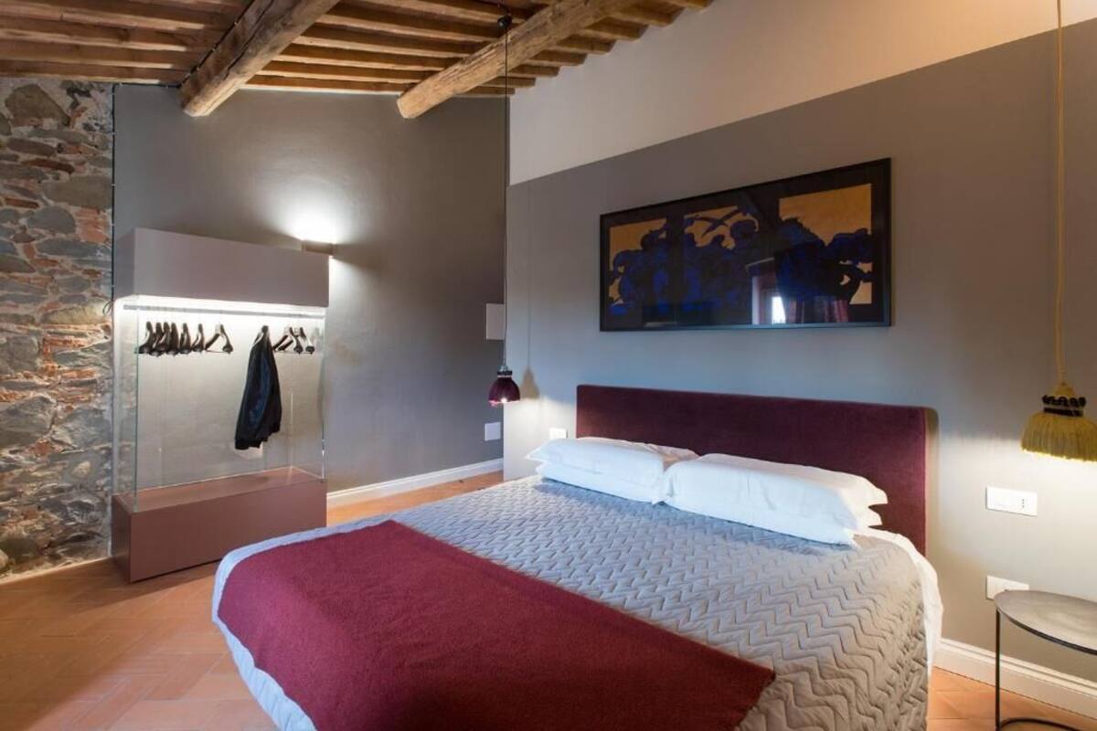 A bedroom with a bed, a wall-mounted artwork, a coat rack, and a stone wall.