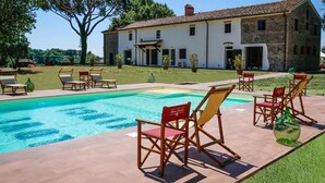 Una piscina con sillones de descanso, un edificio de piedra y un árbol grande.