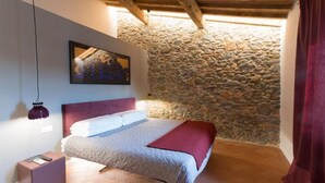 Un dormitorio con pared de piedra, cama con cabecera roja, lámpara colgante y un cuadro enmarcado en la pared.